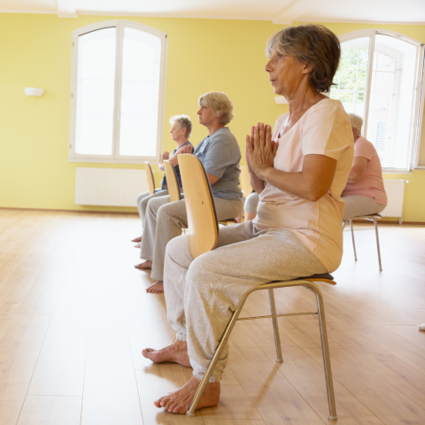 People sitting on chairs with their hands in the namaste position 