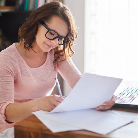 Woman wearing glasses looking at a paper while sitting at a desk