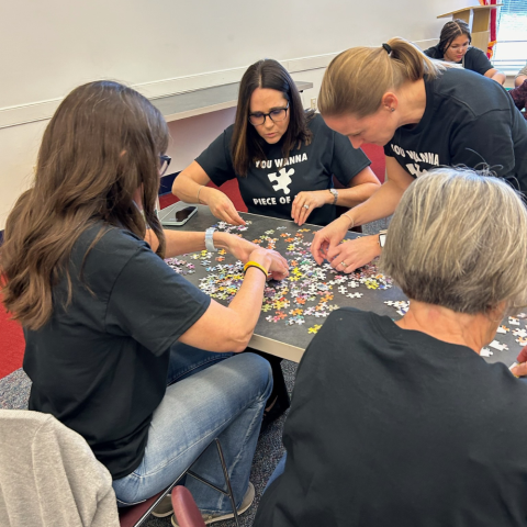 Photo of a group of women hunched over a table putting together a puzzle