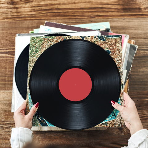 Photo of woman's hands holding a vinyl record at the top of a stack of records