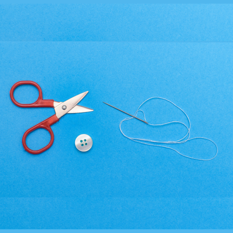 scissors, button, needle and thread against a blue background