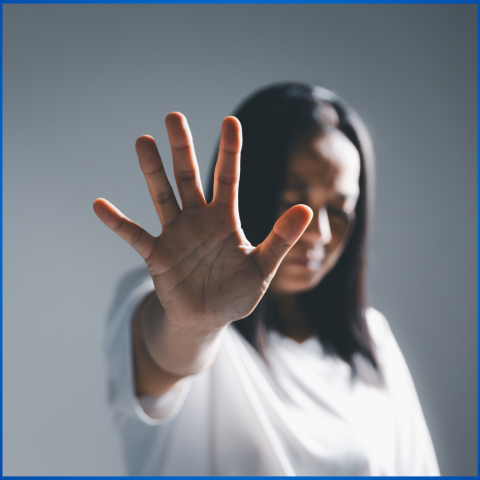 Photo of a woman against a gray background with her arm raised up and her open palm facing the camera