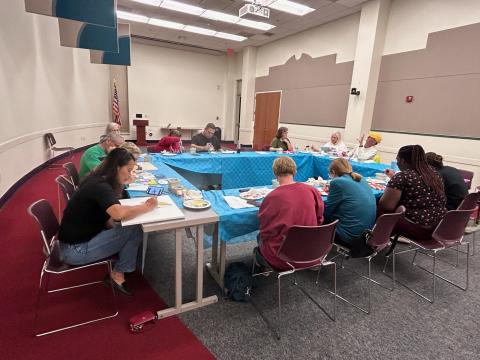 People sitting around a set of tables arranged in a rectangle while working on painting projects