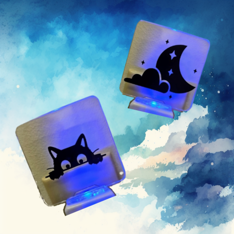 Two clear nightlights, each with a black vinyl design and a lit-up blue light against a background. The background looks like blue and gray watercolor blooms on white.