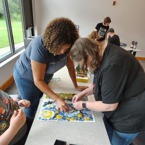 Two people bent over a table putting together a jigsaw puzzle