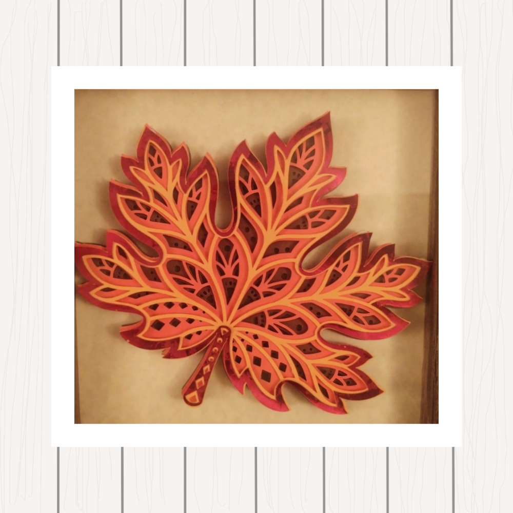 Photograph of autumn leaf made of paper layers against a white wood background