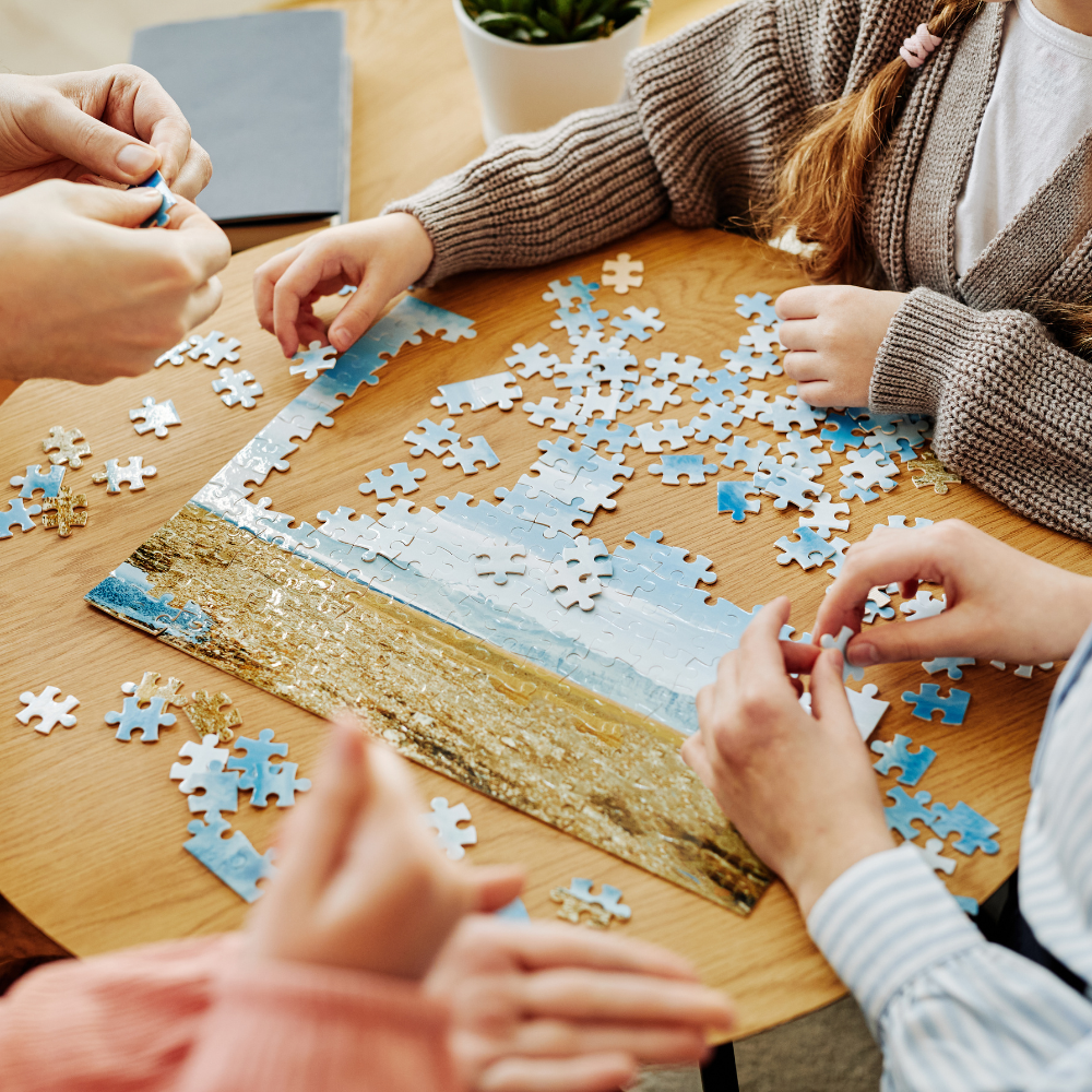 Photo of a group of people hunched over a table putting together a puzzle